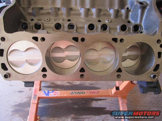 Engine block with four pistons visible, mounted on an orange stand