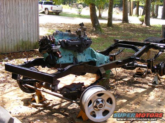 Vehicle frame with engine and a white pickup truck in the background