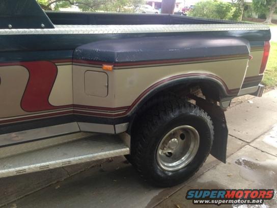 Rear side of a tan and blue Ford F-Series truck with red stripe graphics. Dual rear wheels visible