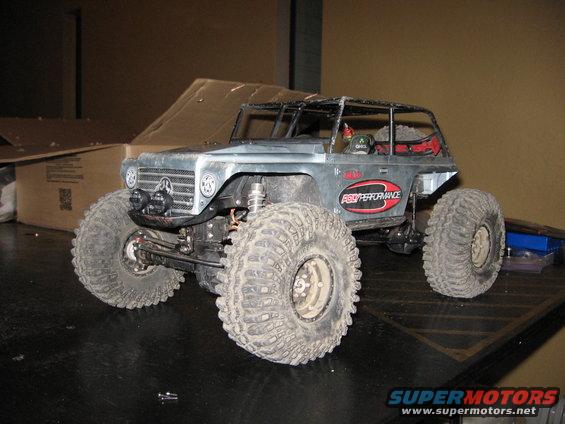 Silver remote control rock crawler with large tires and a roll cage, parked on a dark surface