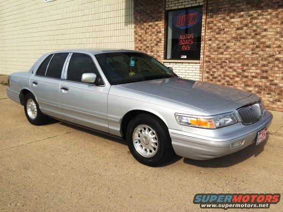 Silver 1995 Mercury Grand Marquis parked outside a building with an 'Open Autos Boats RVs' sign