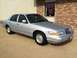 1995 Mercury Grand Marquis - A silver 1995 Mercury Grand Marquis is parked in front of a brick building with a sign in the window.