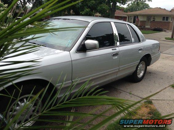 Silver 1995 Mercury Grand Marquis sedan parked on a driveway, partially obscured by palm fronds