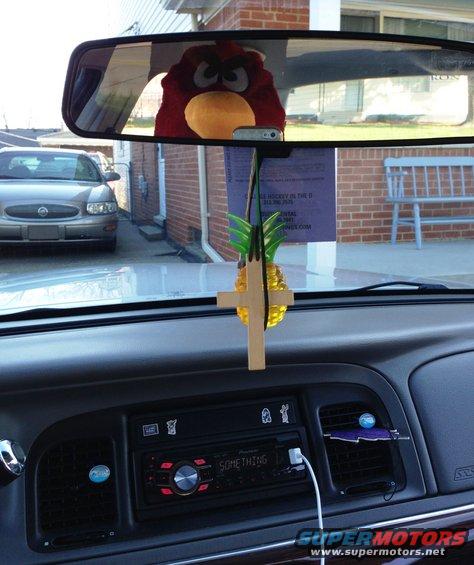 Car interior showing dashboard, Pioneer stereo, and a stuffed toy reflected in the rearview mirror. Another car is visible outside