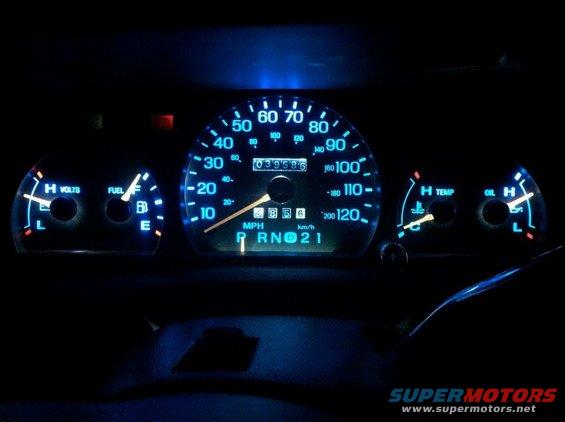 Car dashboard with glowing blue gauges, showing fuel, volts, speed, temp, and oil levels. Odometer reads 039596