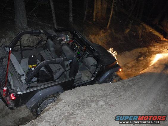 2005 Jeep Wrangler tilted on a dirt embankment at night, with headlights illuminating the scene