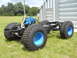 1992 Ford Bronco - This image shows a vehicle chassis with oversized tires and a prominent blue engine, set against a grassy backdrop.