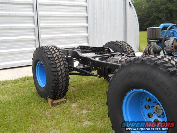 Truck frame with big tires and blue rims, engine visible on right