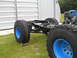 1992 Ford Bronco - The chassis and engine of a vehicle are shown outdoors, with large off-road tires mounted on blue wheels.