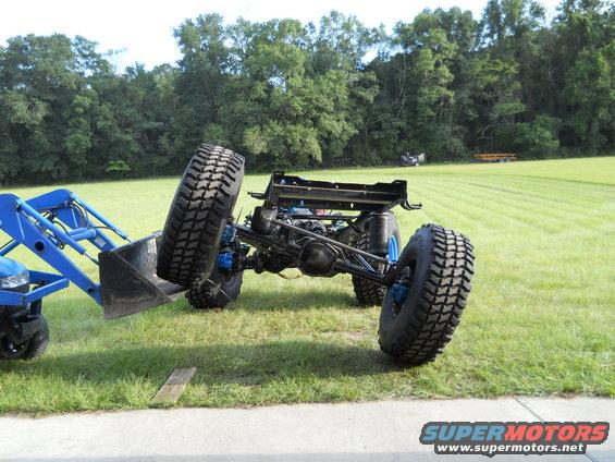 Blue tractor loader lifting a vehicle chassis with large tires