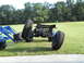 1992 Ford Bronco - A tractor loader is lifting the chassis of a vehicle with large off-road tires.