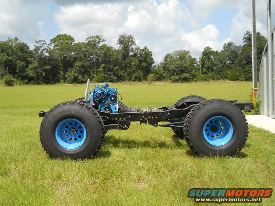 Truck chassis with blue engine and large tires with blue rims, side view