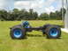 1992 Ford Bronco - A truck chassis with an engine and oversized tires sits on a grassy field under a cloudy sky.