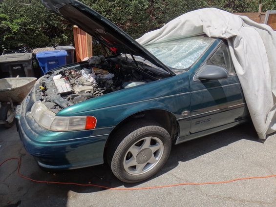 green sedan, hood open showing engine, half covered with a tarp