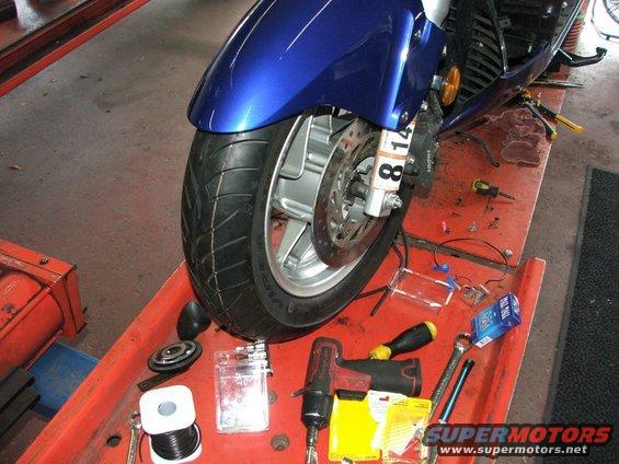 Motorcycle front wheel, brake disc, and caliper assembly on a red service tray with tools