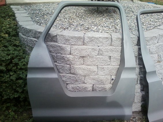 Two gray car doors, one in foreground, leaning against a stone wall