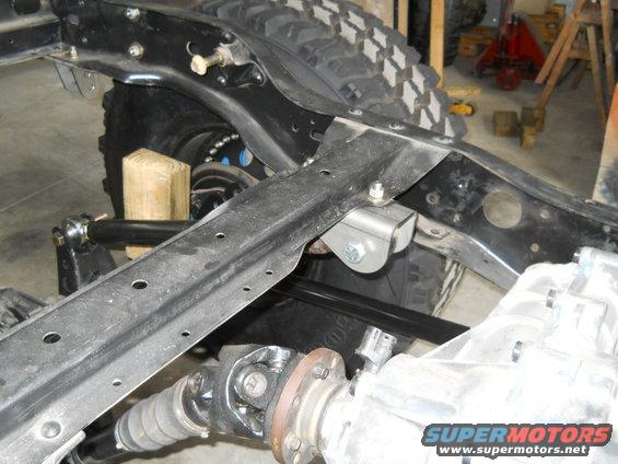 Close-up of vehicle frame with suspension and drivetrain parts visible. Supermotors.net logo in lower right