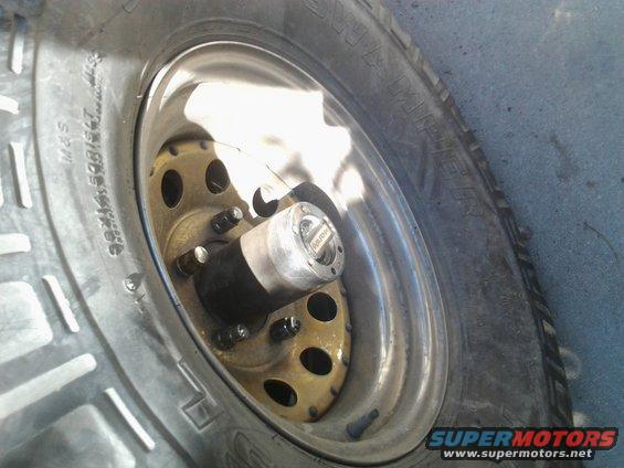 Close-up of a vehicle's wheel hub with a gold-colored rim and a black and silver locking mechanism, next to a tire with visible tread