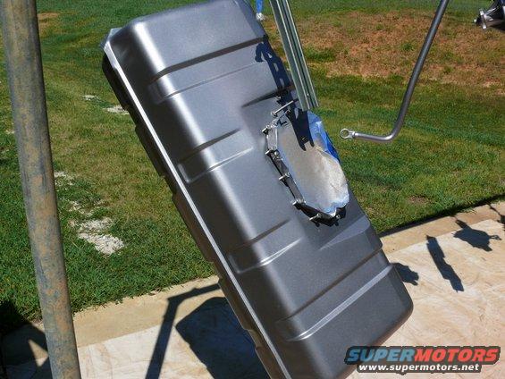 Gray metal fuel tank with a silver mounting bracket attached, angled on a stand outdoors