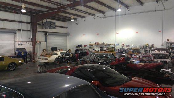 Interior of an auto shop with a yellow car, a white car with engine exposed, a black car, and two jet skis