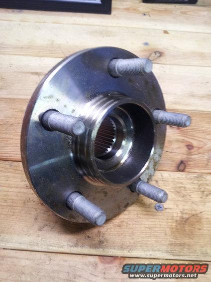 Wheel hub with five lug bolts on a wooden surface. The hub has a splined center bore and shows signs of wear