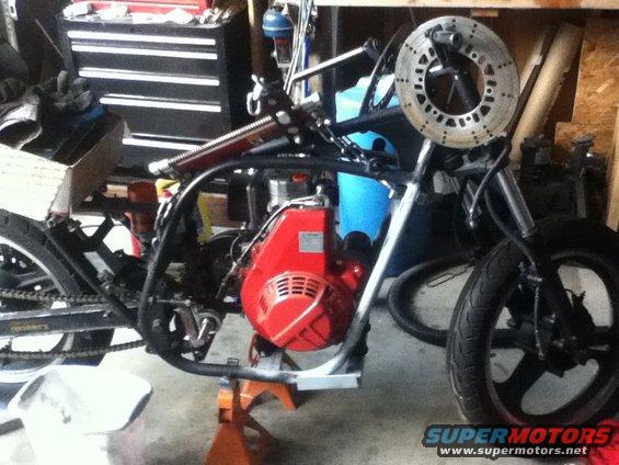 Motorcycle frame with a red engine mounted, front wheel and disc brake visible