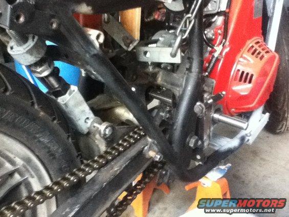 Motorcycle frame with chain and red engine component, close-up view