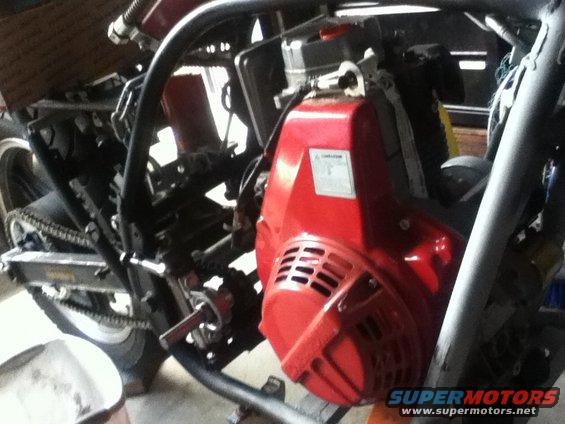 Close-up of a red engine with a label on its side, part of a motorcycle frame visible