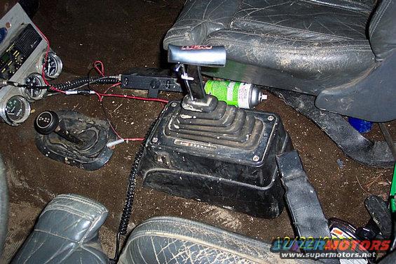 Interior view of a vehicle's floor with dual shifters, gauges, and a spray can