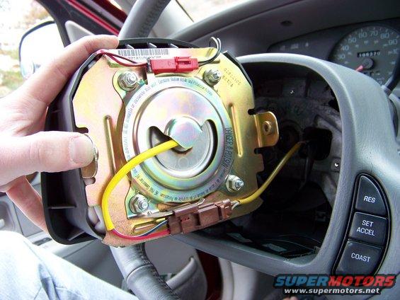 Removing airbag module from steering column, showing wiring and internal components. Dashboard gauges visible