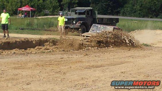 Jeep Wrangler splashing through mud, military truck behind