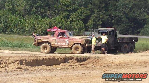 Red pickup truck with a red canopy, mud-splattered, parked next to a military truck