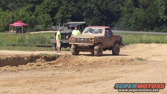 Muddy pickup truck with a tow rope, parked next to a military truck. Two guys stand between them