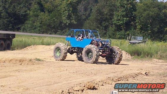 Blue buggy with large tires and roll cage, being towed by a trailer