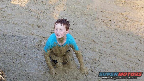 Boy in blue shirt covered in mud, sitting in a muddy area