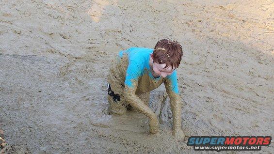 Child in blue shirt and shorts crawling through thick mud