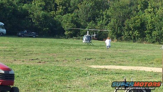 Helicopter on the ground with a person walking towards it, pickup truck parked nearby