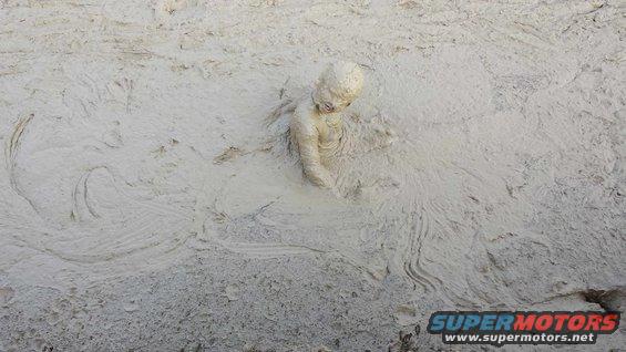 person covered in mud, stuck up to their chest in a muddy area