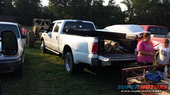White pickup truck with its tailgate down, carrying a white cover and two cylindrical objects