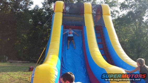 Inflatable slide with yellow and blue sections, a boy sliding down, and trees in the background