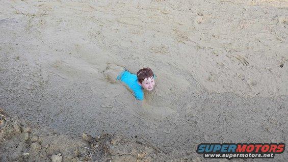 Child in blue shirt stuck in mud, smiling at the camera