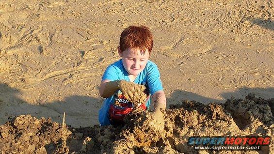 Child playing with red toy truck in mud