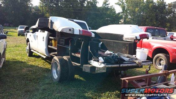 dual rear wheel pickup truck with utility body and a white cap on the bed, parked next to a red pickup truck