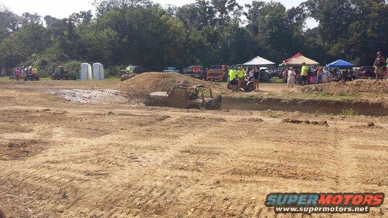 off-road vehicle stuck in mud pit with spectators watching