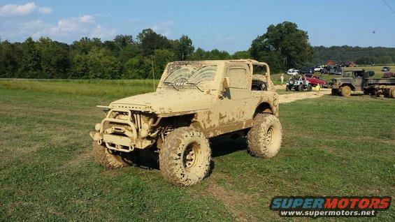 Mud-covered Jeep Wrangler with large tires parked on grass