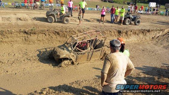 Mud-covered off-road buggy stuck in a mud pit with spectators watching