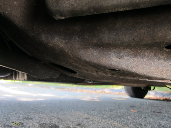 Underside of a car showing frame and suspension components. A tire is visible on the right