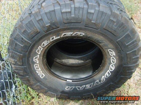 Close-up of Goodyear Wrangler tires stacked up, with a chain-link fence in the background
