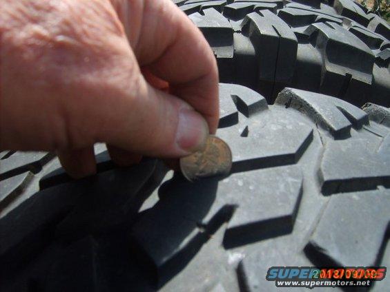 Hand holding coin to show tread depth on a large off-road tire