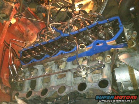 Close-up of engine valve cover with blue gasket and intake manifold components